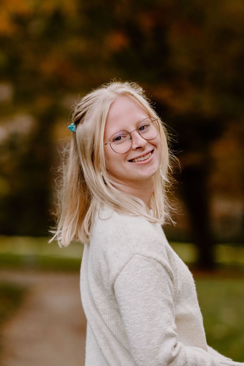 A person with blonde hair wearing a white sweater laughs joyfully in an autumn outdoor setting.