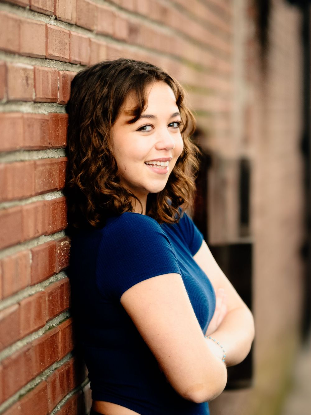 Three connected portrait shots with blue dress against red brick wall show candid poses in natural light.