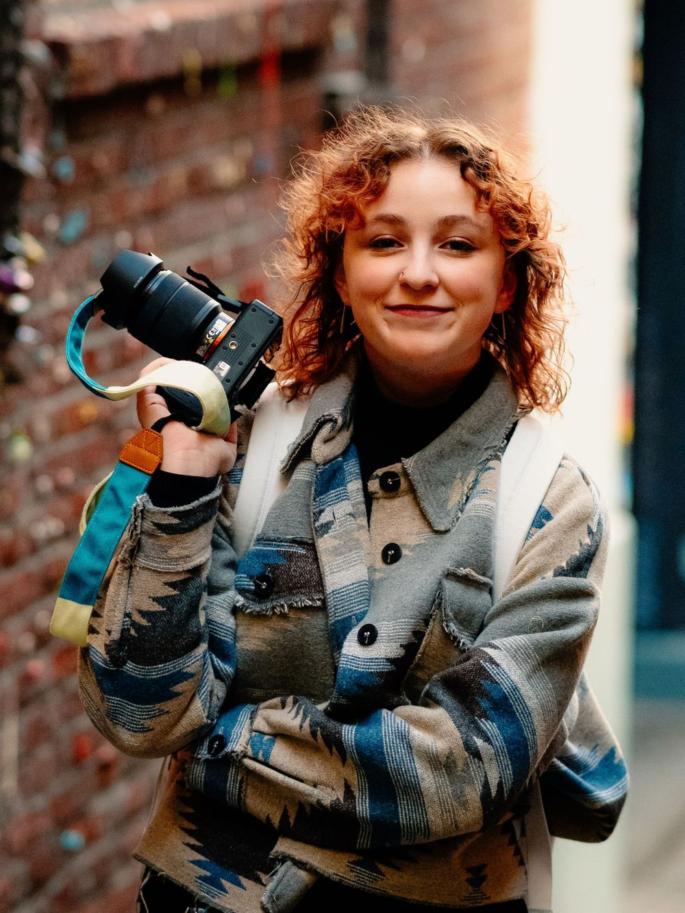 A person in a gray coat with curly hair poses playfully in a series of four similar shots against a brick wall.