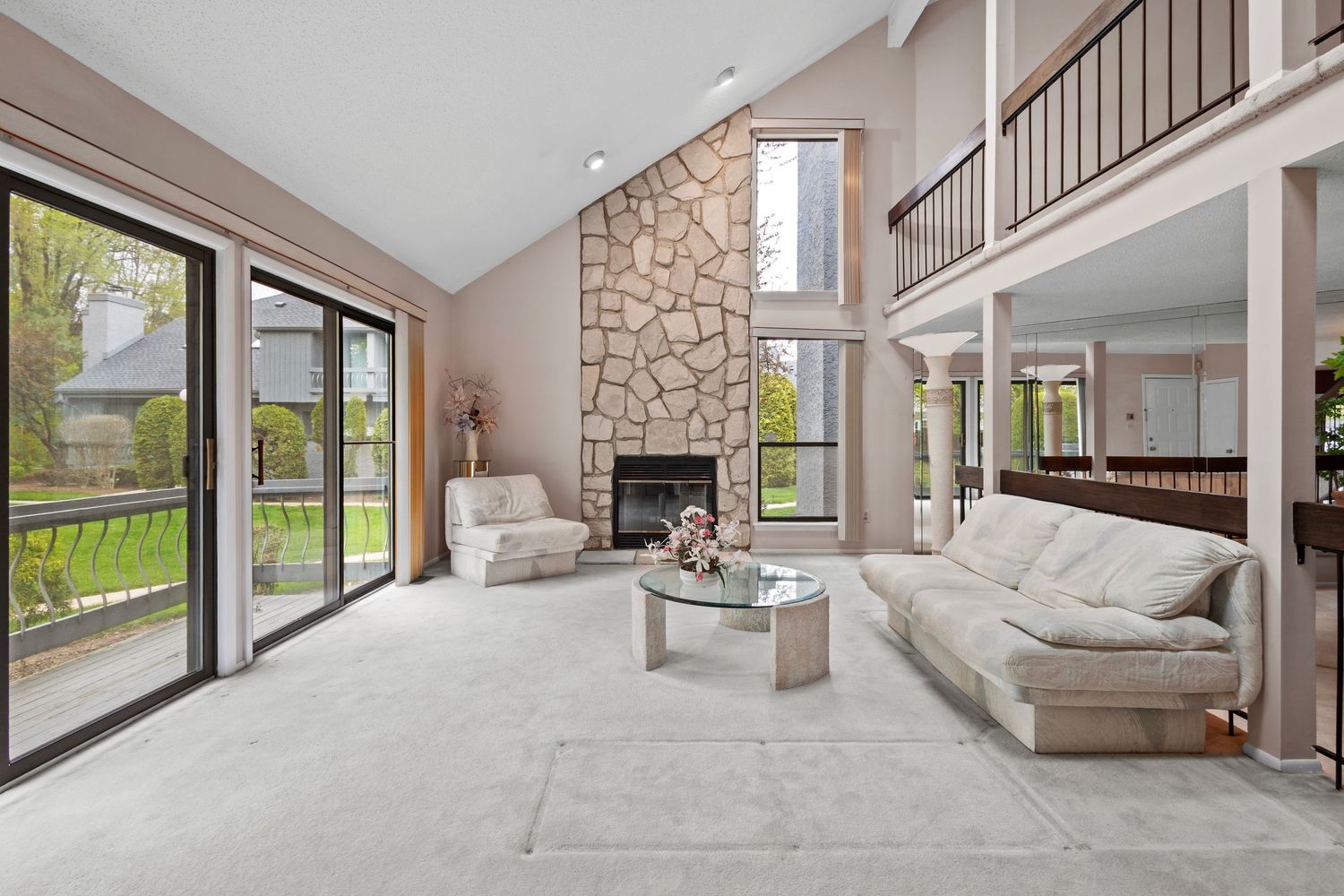 Modern living room with floor-to-ceiling stone fireplace, white couches, and sliding glass doors overlooking natural landscape.