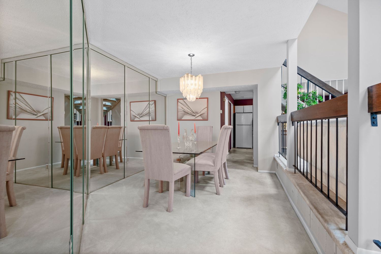 Modern dining area with mirrored wall features upholstered chairs, crystal chandelier and neutral tones throughout.