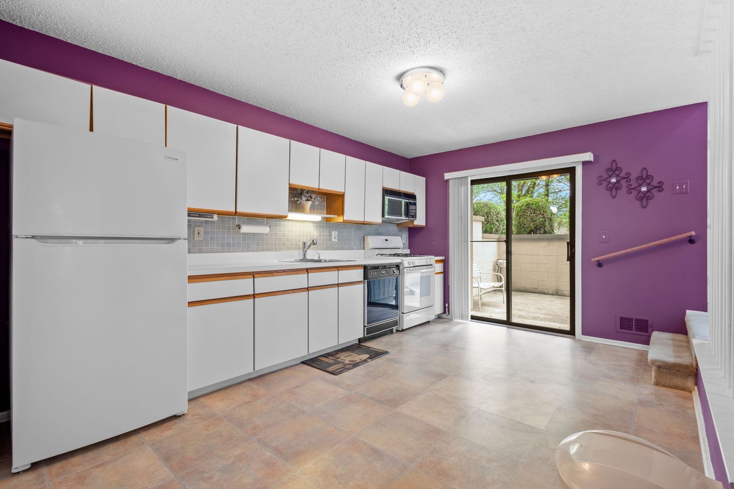 Modern kitchen space with purple accent wall features bright white cabinets and sleek tile flooring.