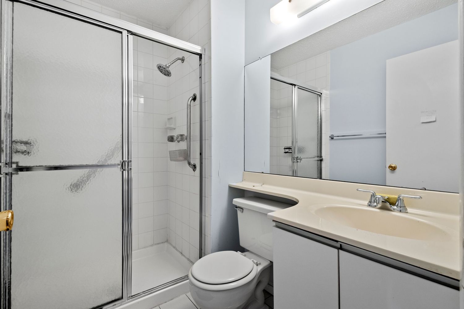 Modern bathroom with white vanity counter, toilet and glass-enclosed shower stall featuring chrome fixtures and beige countertop.