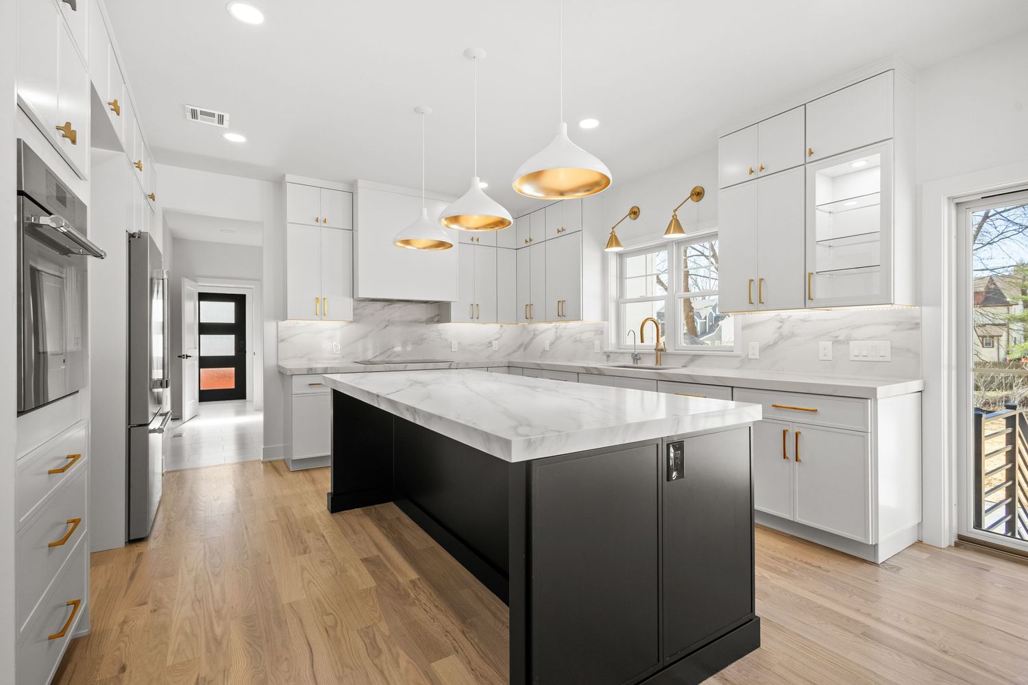 Bright open concept kitchen and dining space with white cabinets and black island extending down hallway.