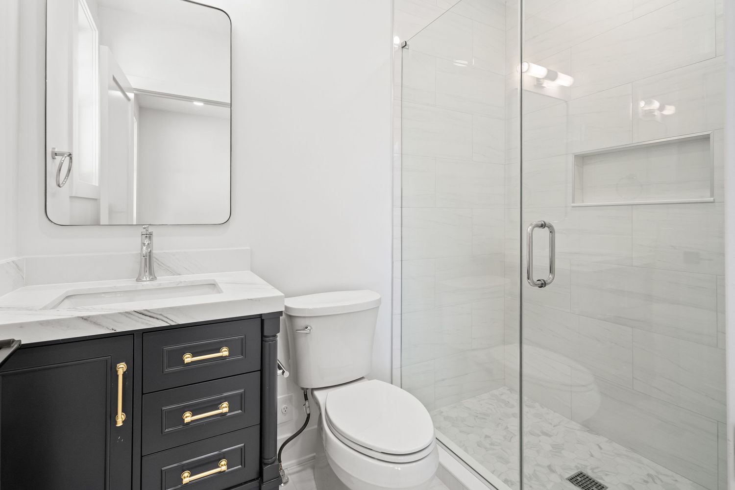 Luxurious white marble bathroom featuring frameless glass shower enclosure and gold fixtures.
