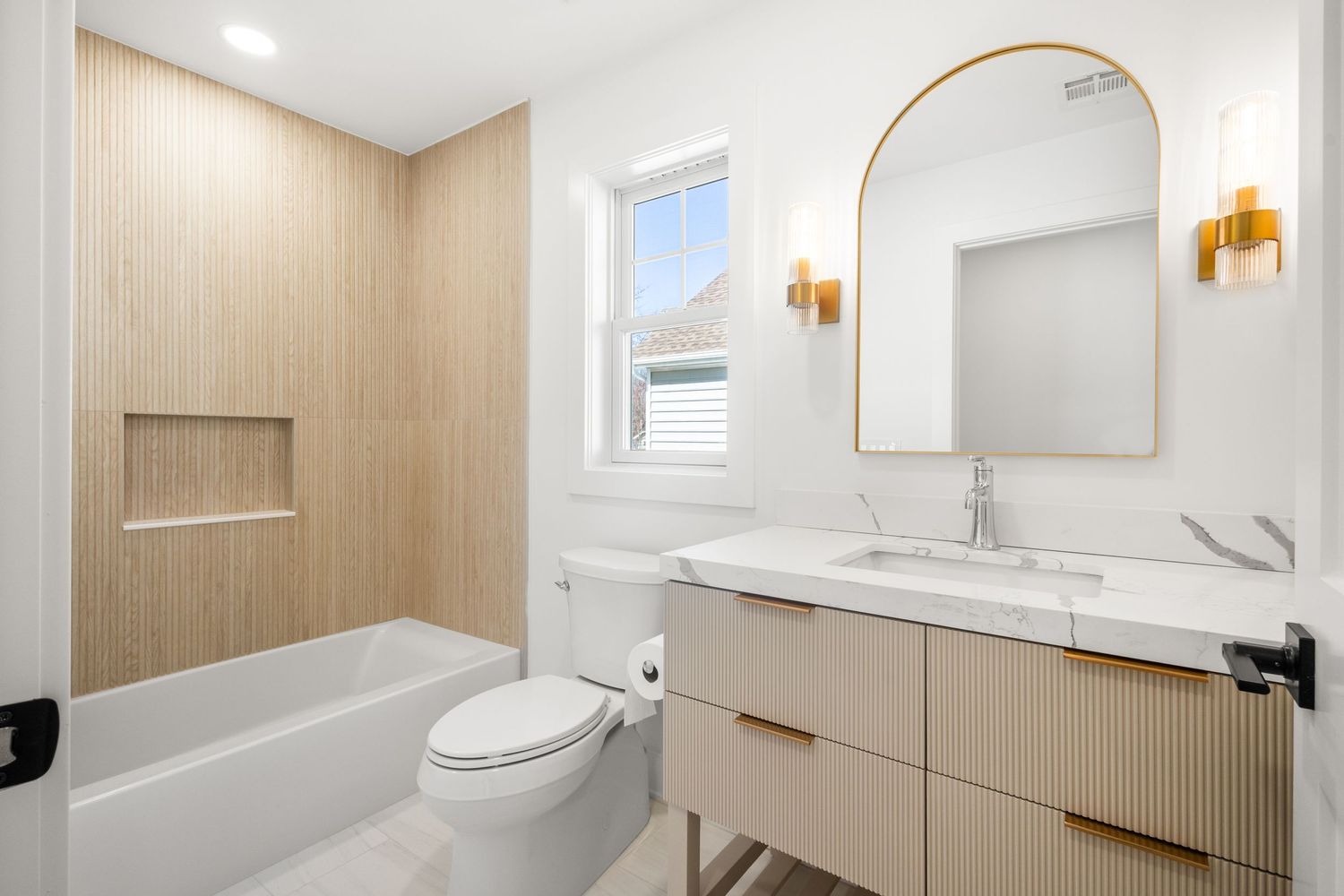 Contemporary bathroom with freestanding tub, wood accent wall, and modern sconce lighting.