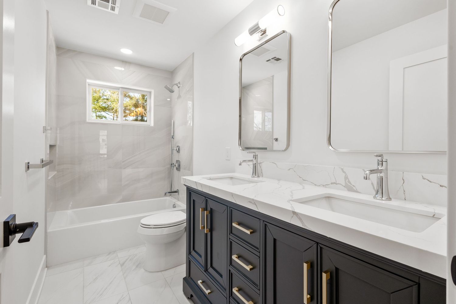 Modern bathroom features dark navy vanity with white quartz countertop, dual sinks and marble tile shower enclosure.