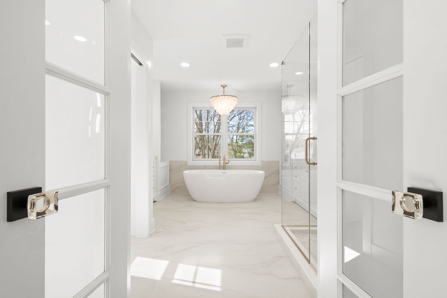 Spacious white hallway with natural light streaming through windows and modern light fixtures.
