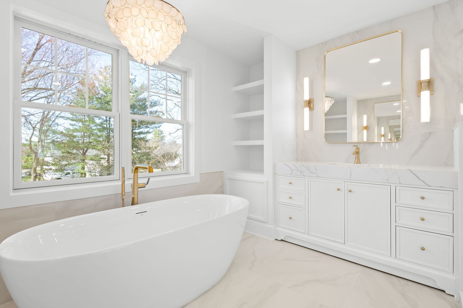 Luxurious white bathroom featuring a freestanding tub, chandelier, and large windows with natural light.