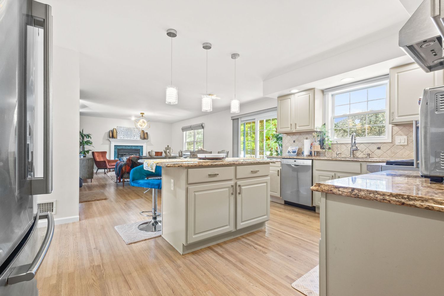 Modern white kitchen with hardwood floors, quartz countertops, and stainless steel appliances opens to bright living area.