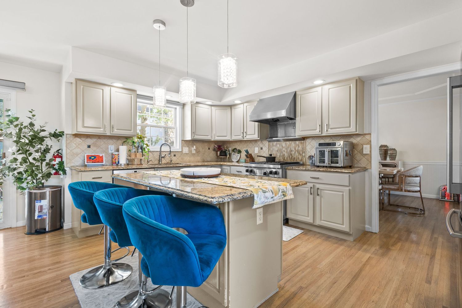 Modern kitchen with gray cabinets, wood floors, and bright blue velvet barstools at white island with pendant lighting.