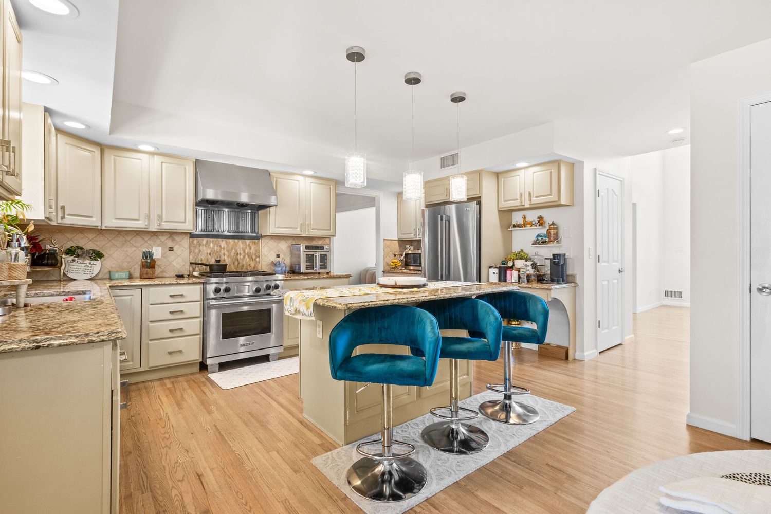 Modern open concept kitchen with light wood cabinets, stainless appliances and turquoise bar stools at breakfast counter.