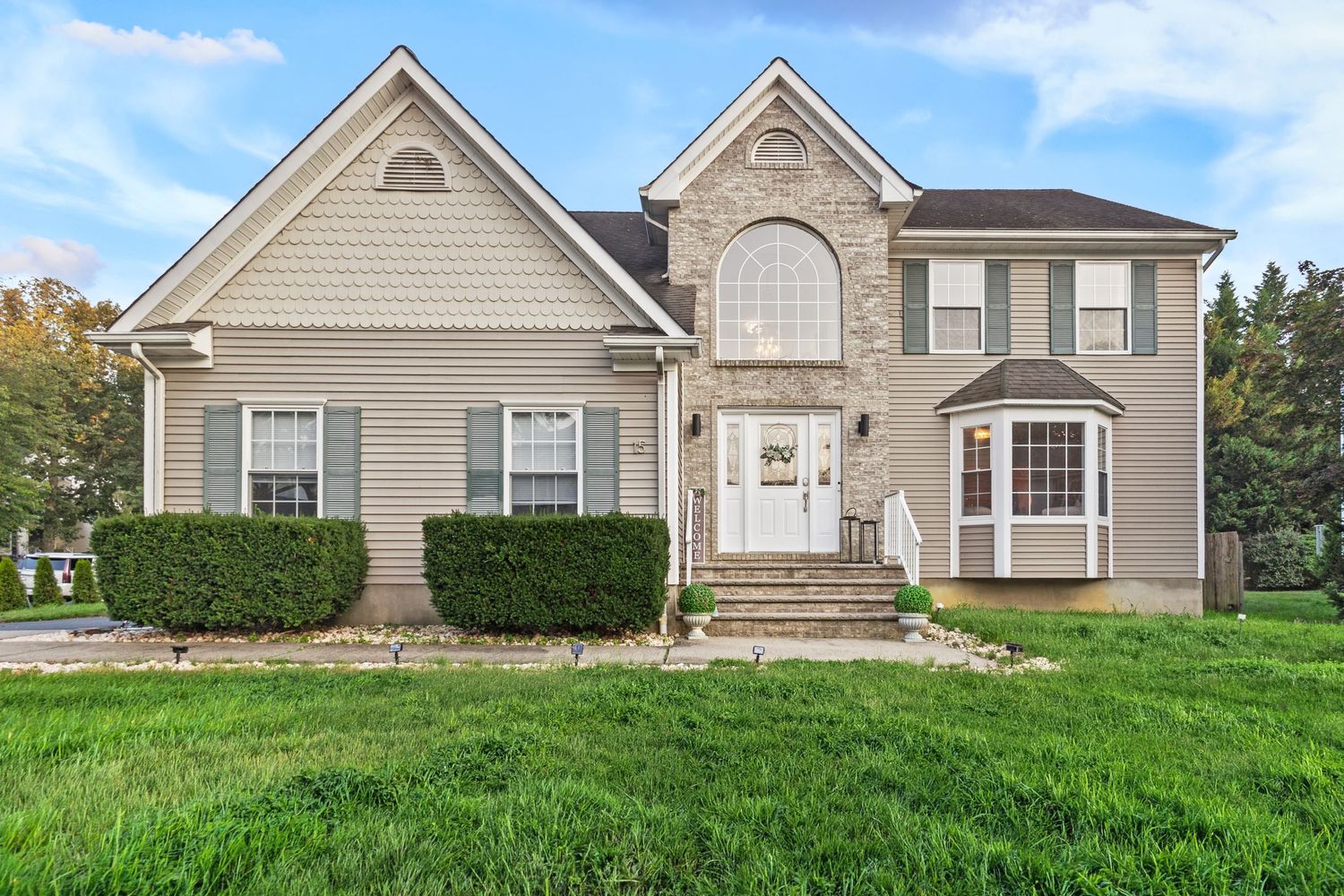 Two-story suburban home with beige siding, stone accents, bay window, and lush green lawn.