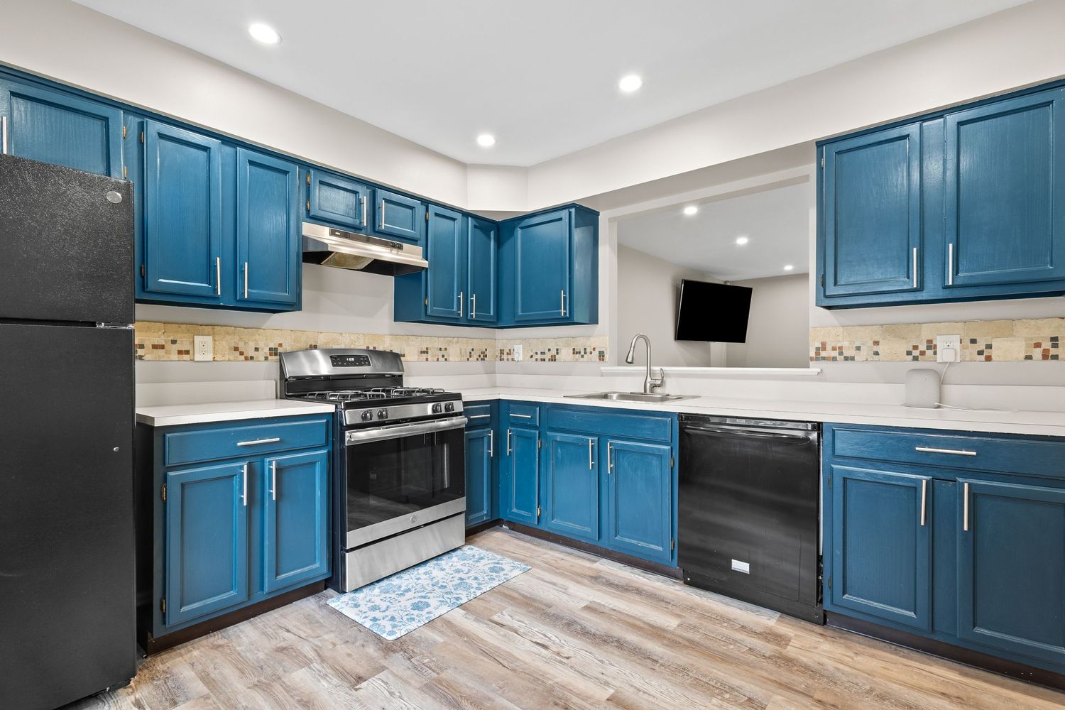 Modern kitchen with bold blue cabinets, stainless steel gas range, black refrigerator, and light hardwood floors.