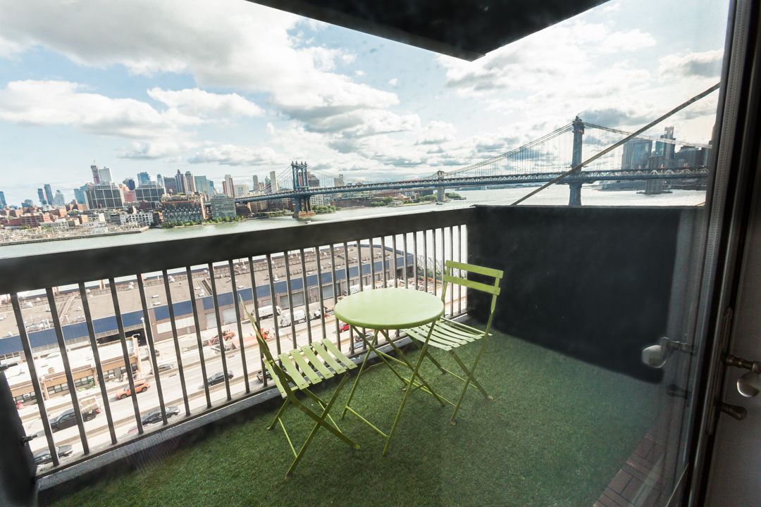 Urban balcony view with green chairs overlooking city skyline and bridge.