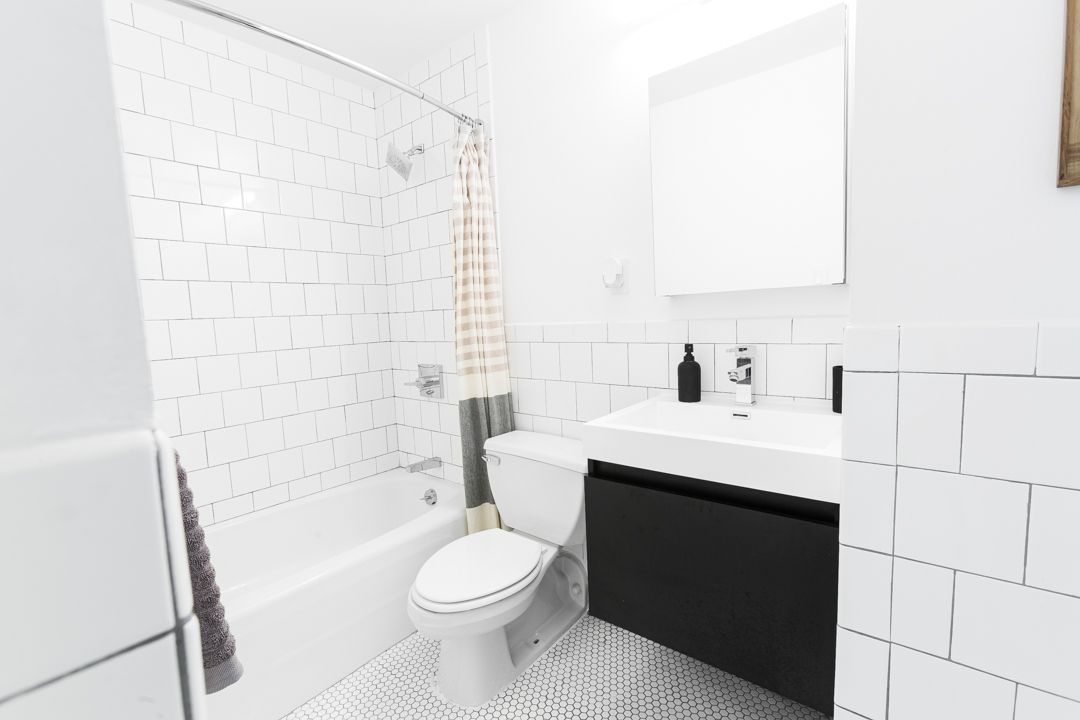 Clean minimalist bathroom with black vanity, white tile walls, and hexagon floor tiles.