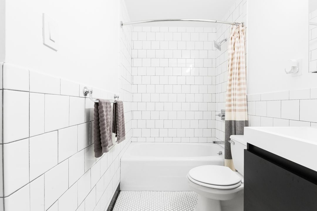 Modern white bathroom with subway tile walls, grey towels, and a striped shower curtain.