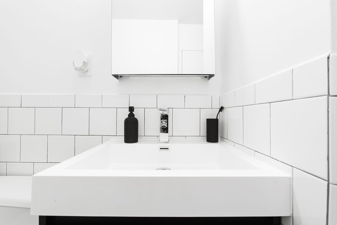 Close-up of modern white sink with black toiletry bottles on black floating vanity.