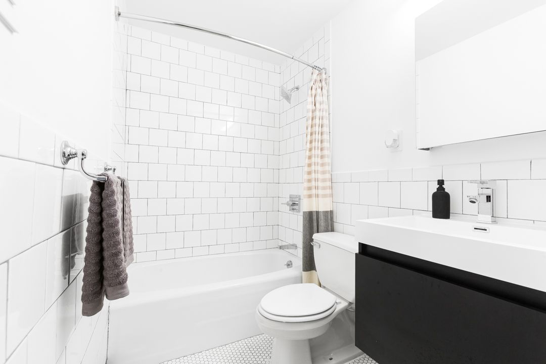 Bright bathroom with white tile walls, floating black vanity, and gray and peach shower curtain.