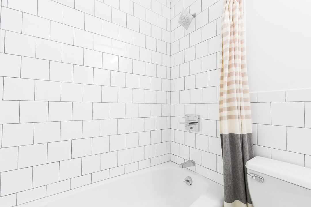 White tiled bathroom showing chrome fixtures and gray and striped shower curtain.