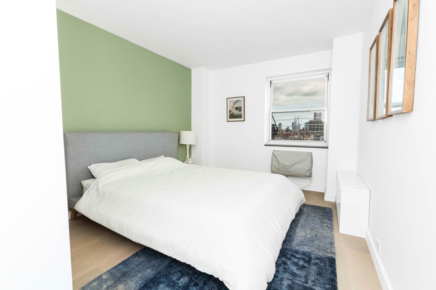 Contemporary bedroom with sage green accent wall, gray headboard and navy area rug.