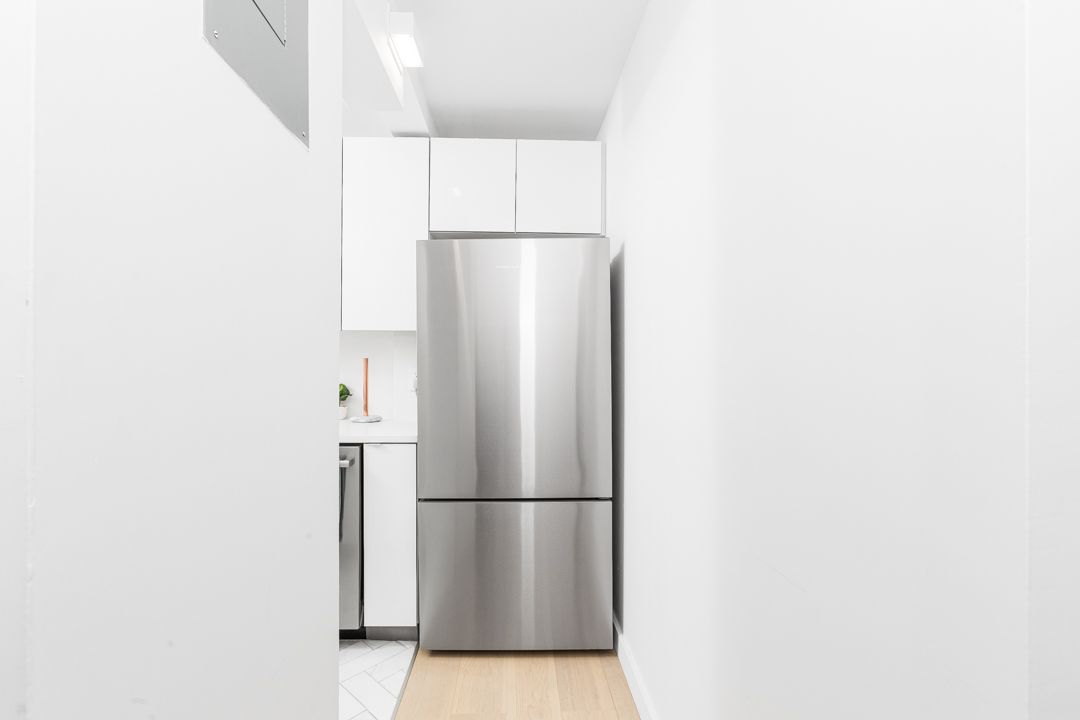 Minimalist white hallway with stainless steel refrigerator and light wood floors.