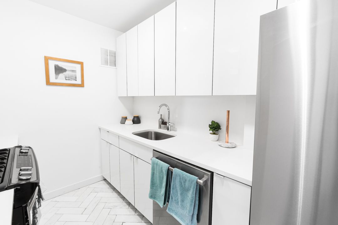 Modern white galley kitchen with sleek cabinets, stainless appliances and a teal dish towel accent.