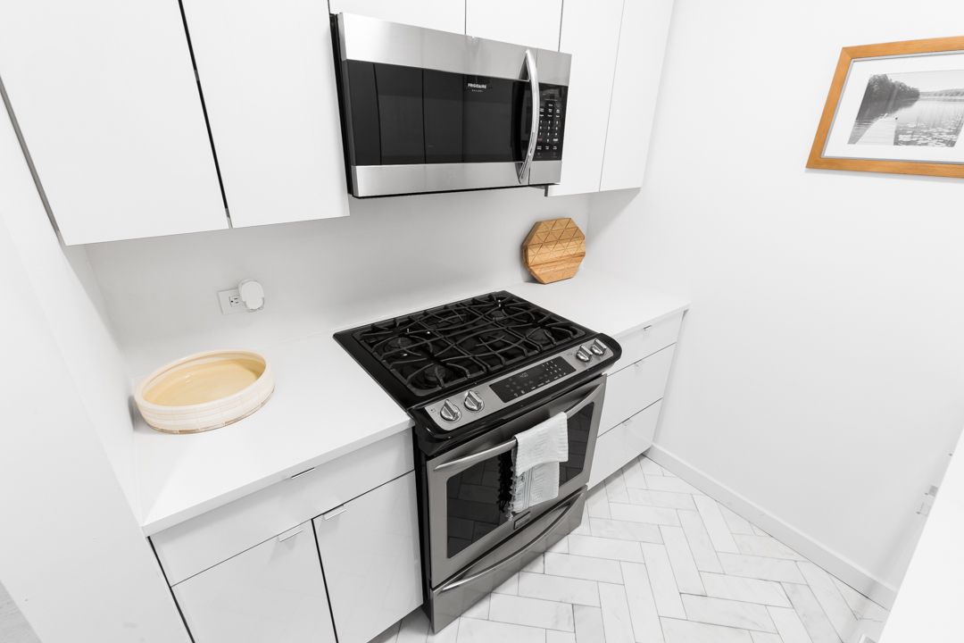 Clean white kitchen featuring black stainless steel appliances and herringbone tile flooring.