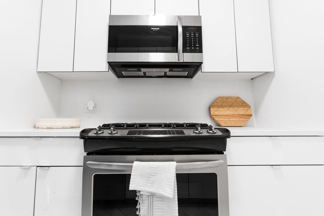 Close-up view of black gas range and microwave mounted between white kitchen cabinets.