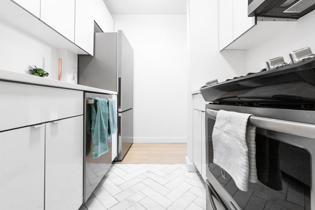 Galley kitchen with white cabinetry, stainless steel appliances and herringbone pattern floor.