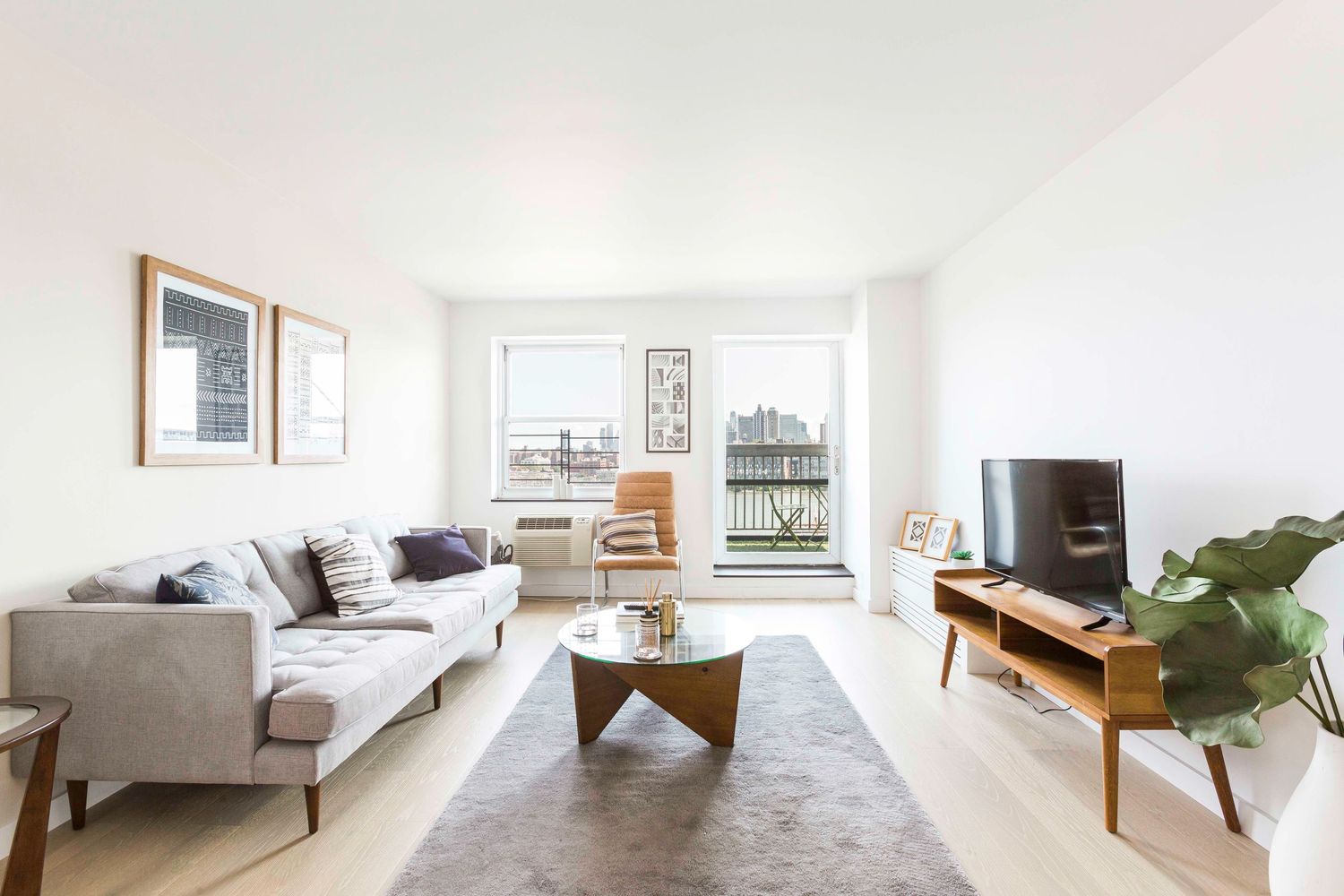Airy living room with gray sectional, geometric coffee table and city views through large windows.