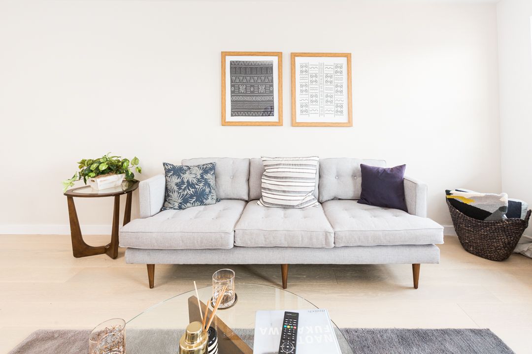 Modern living room interior with gray sofa, framed artwork, and decorative pillows against white walls.