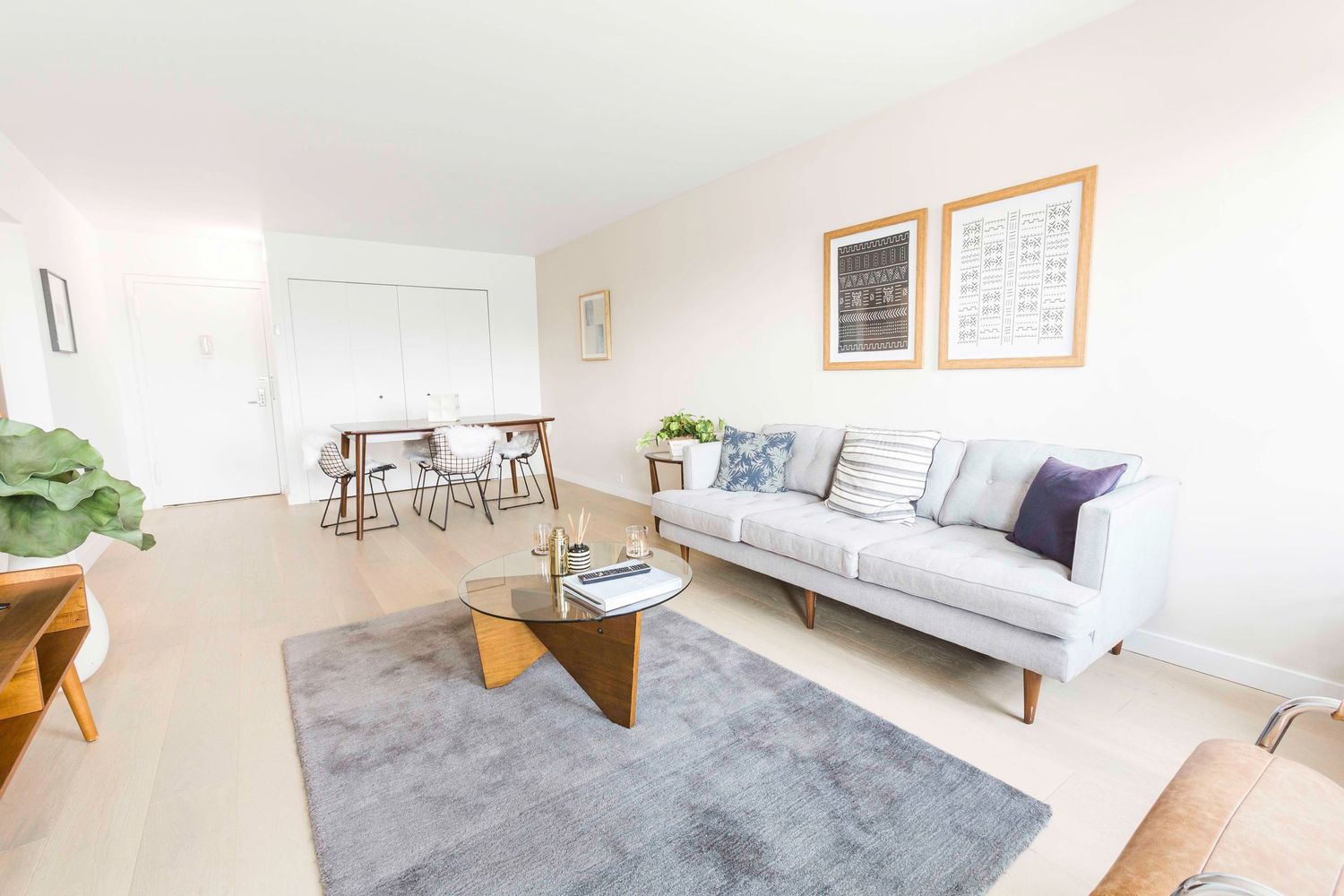Minimalist open concept living room with gray couch, wooden coffee table, and dining area in background.