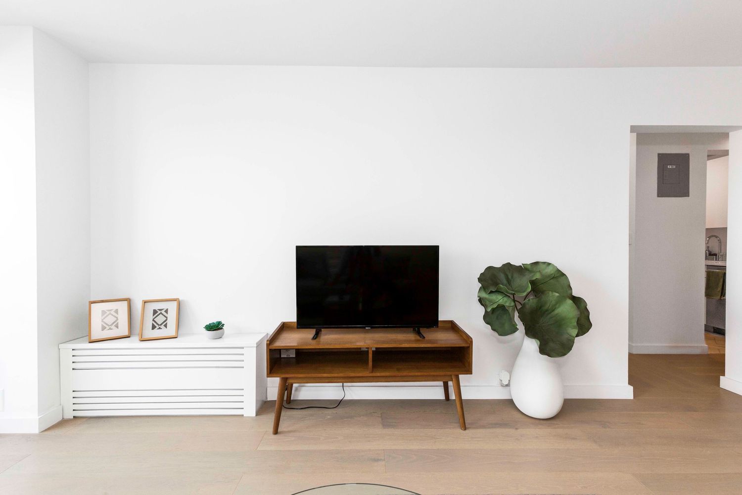 Contemporary TV setup with wooden media console and potted plant against white walls.