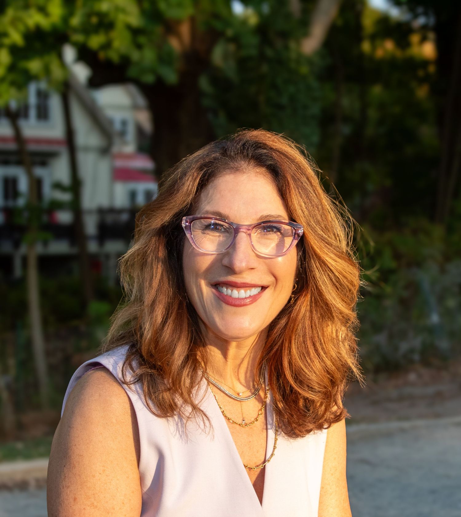 Natural light portrait wearing glasses and sleeveless top with trees in background.
