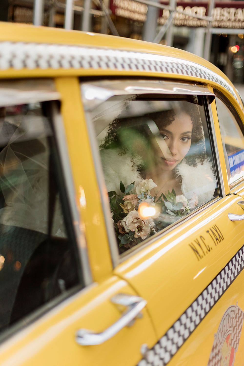 A classic yellow NYC taxi on the street with a passenger looking through the window, holding a bridal bouquet.