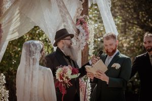 Outdoor wedding ceremony under white fabric arch decorated with pink flowers during intimate garden celebration.