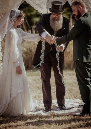 Wedding ceremony participants stand on a white aisle runner during an outdoor autumn celebration.