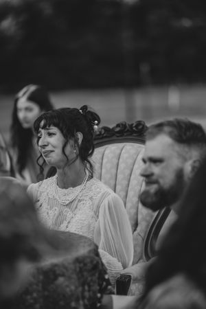 Black and white candid shot of wedding guests seated on vintage furniture at an outdoor celebration.
