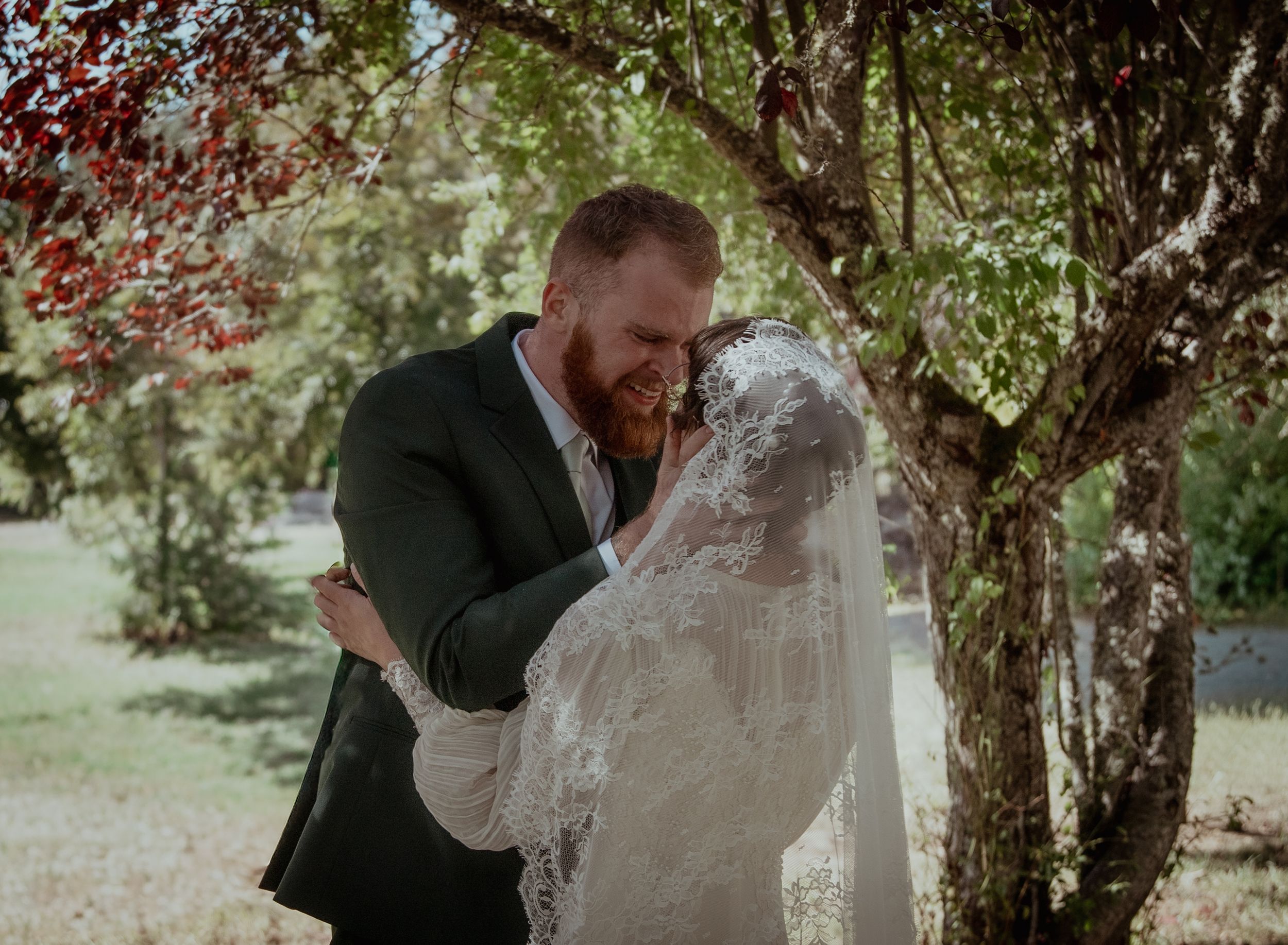 A romantic outdoor wedding moment captured under blooming trees in a garden setting.