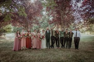 Wedding party poses for a panoramic group photo under autumn trees with burgundy and neutral color scheme.