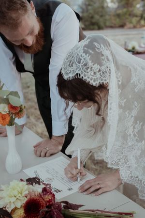 Wedding couple signs marriage documents on a decorated table with floral arrangements.