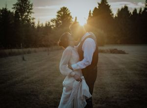 A romantic sunset silhouette of a couple embracing in an open field with evergreen trees.