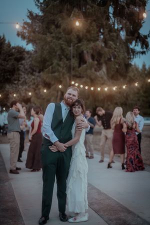 A wedding reception under string lights with guests mingling in the background at dusk.