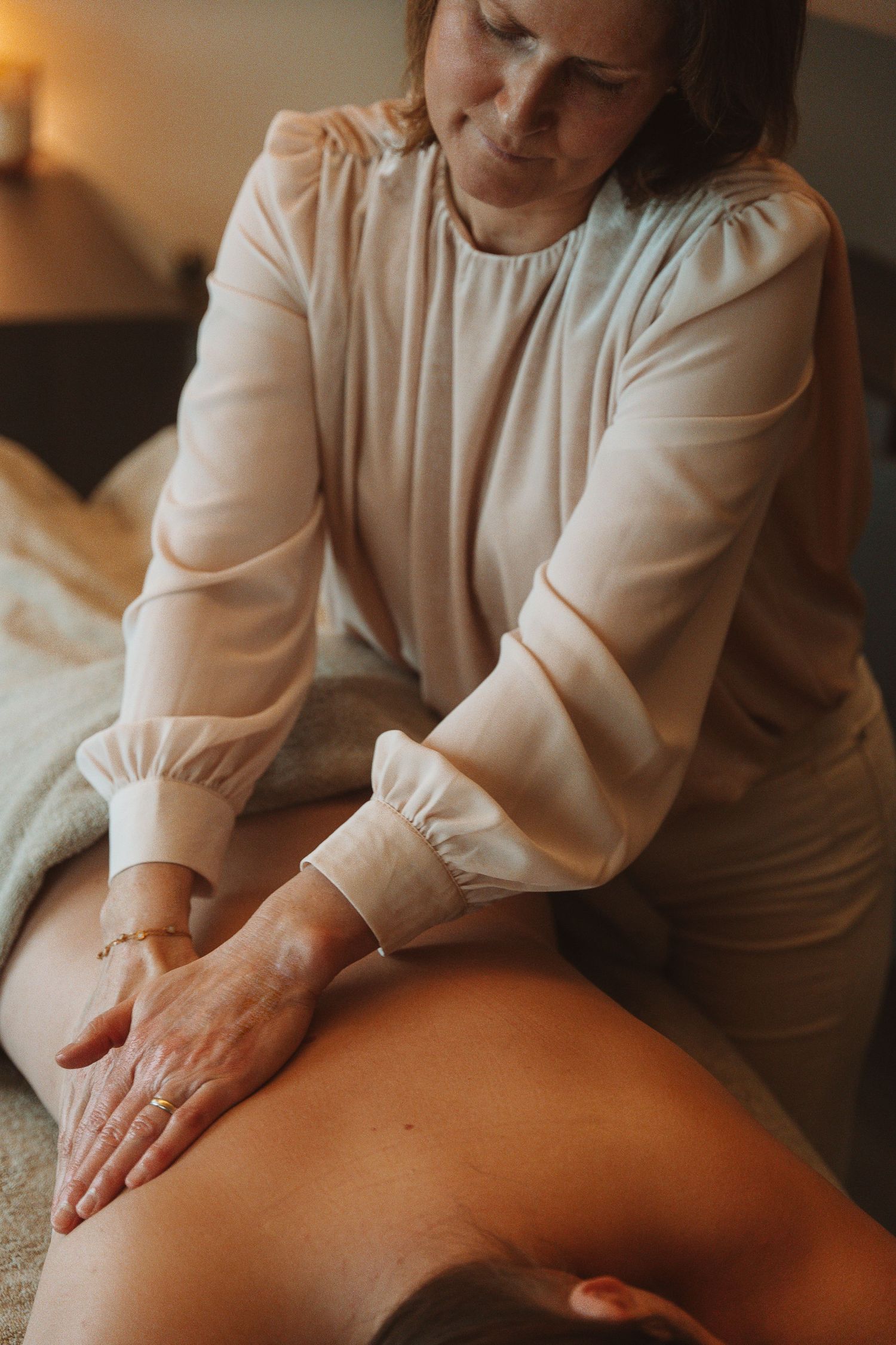 Professional massage therapist performs therapeutic back massage treatment on client in warm ambient lighting.