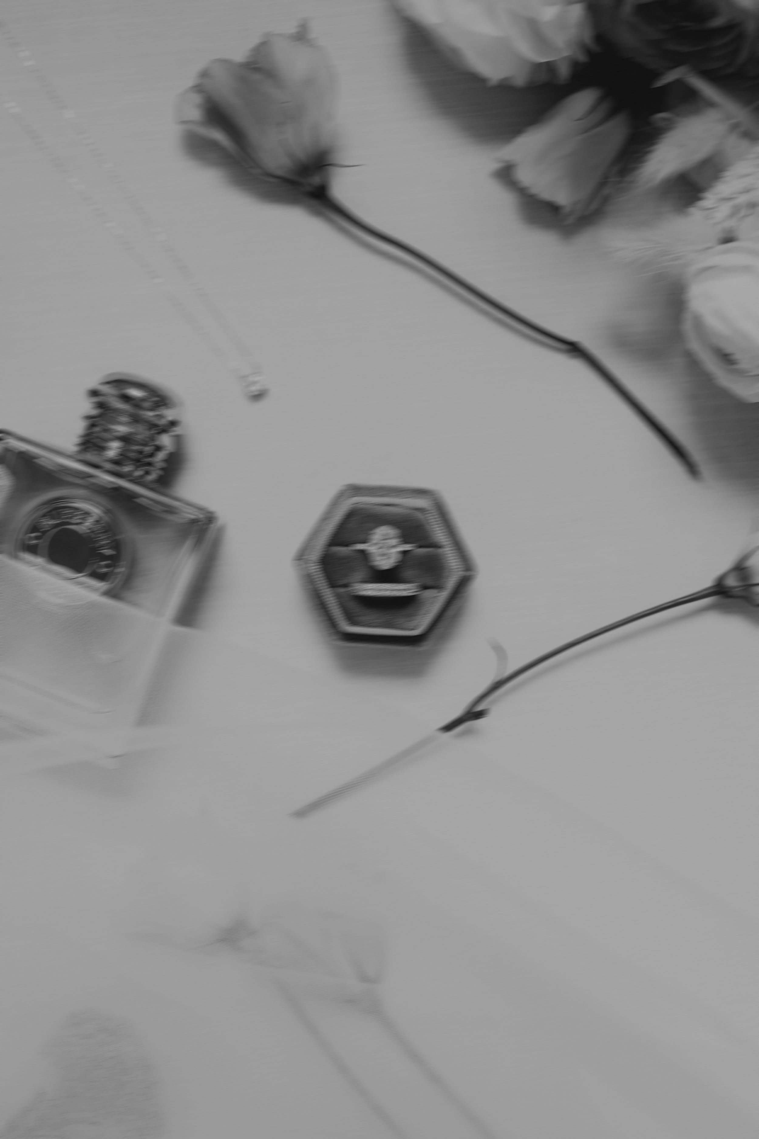 A black and white photo of a perfume bottle and flowers arranged with a hexagonal shape on a marble surface.