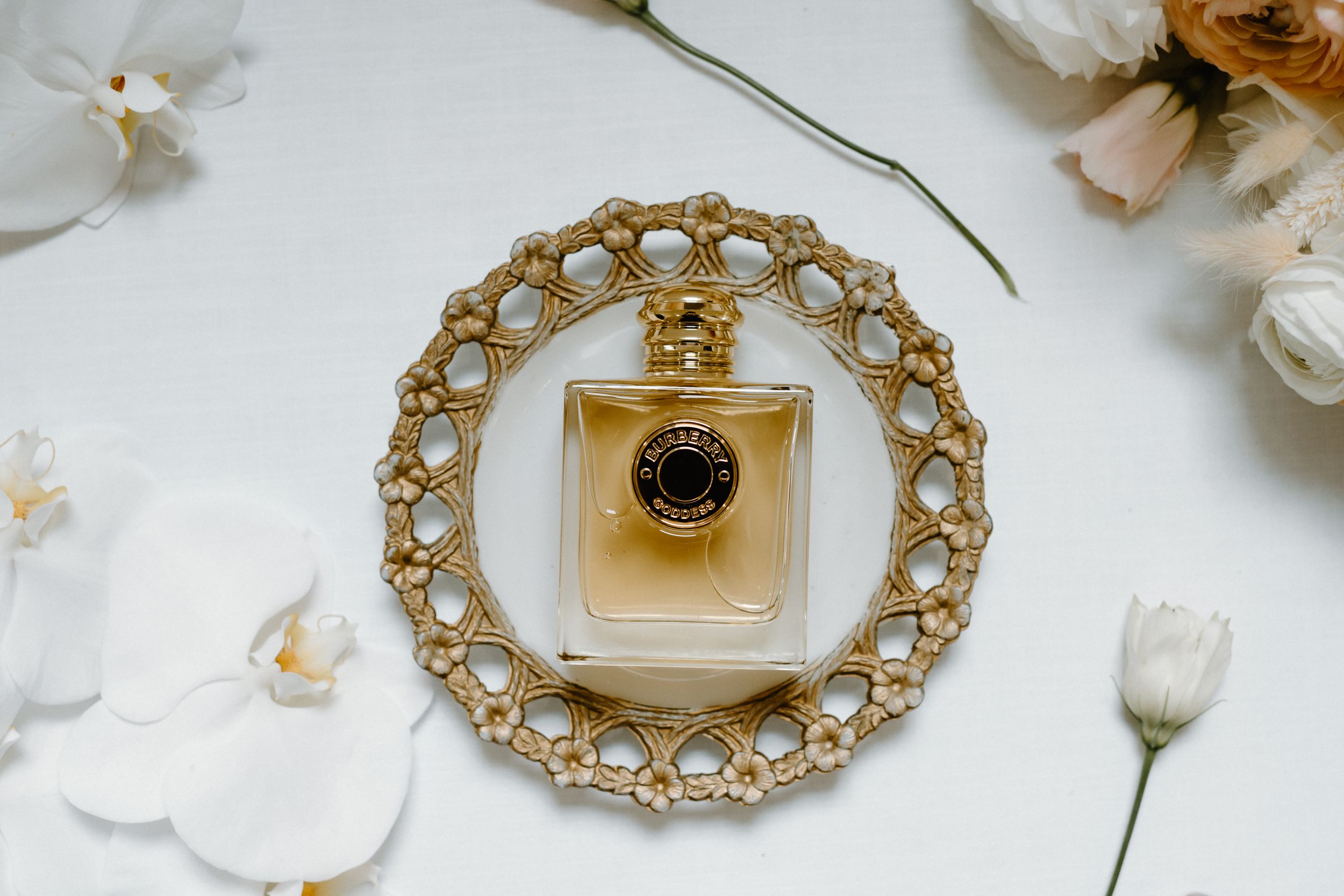 A perfume bottle placed on a decorative gold circular tray with floral accents.