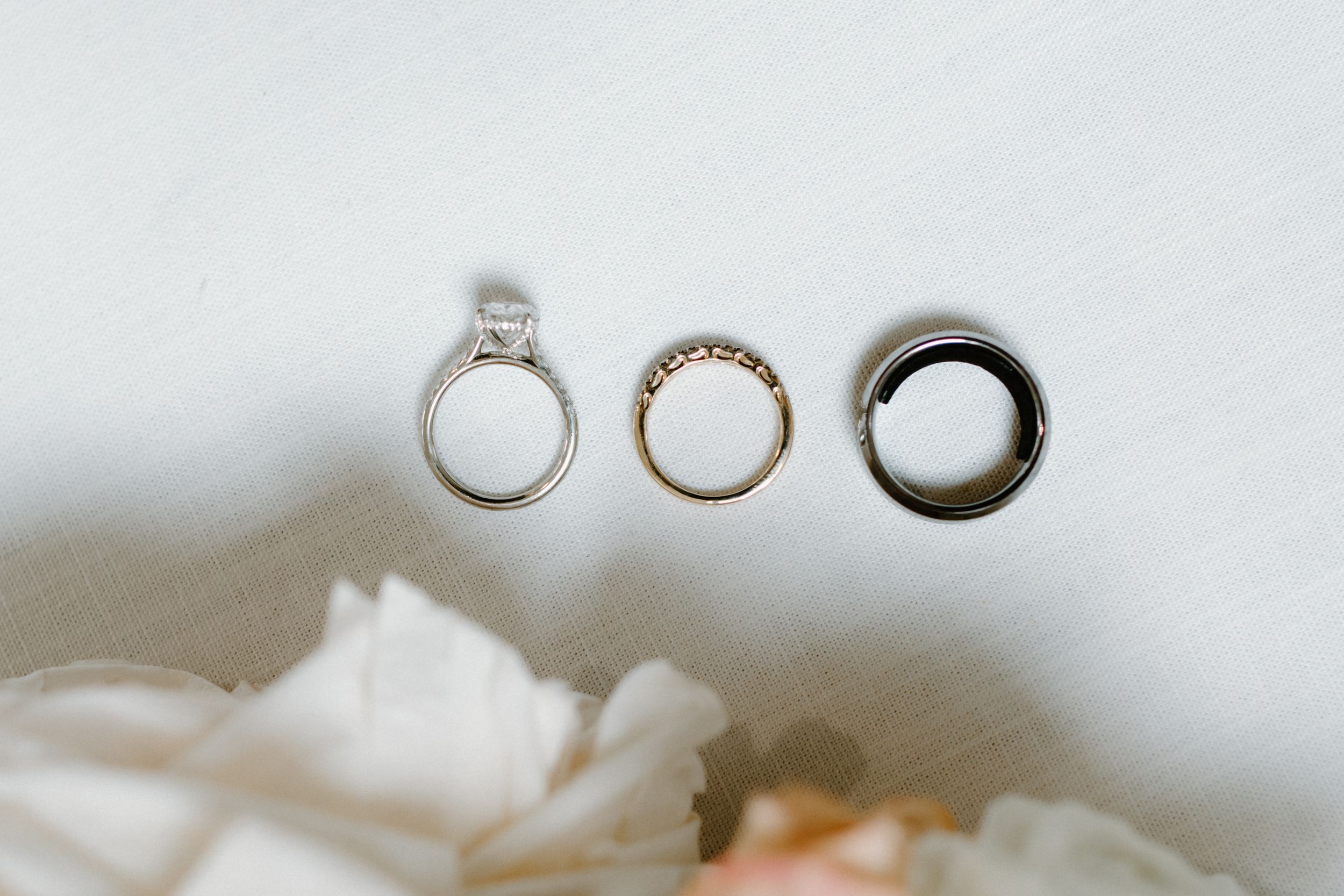 Three wedding rings arranged artistically on white fabric with soft floral elements.