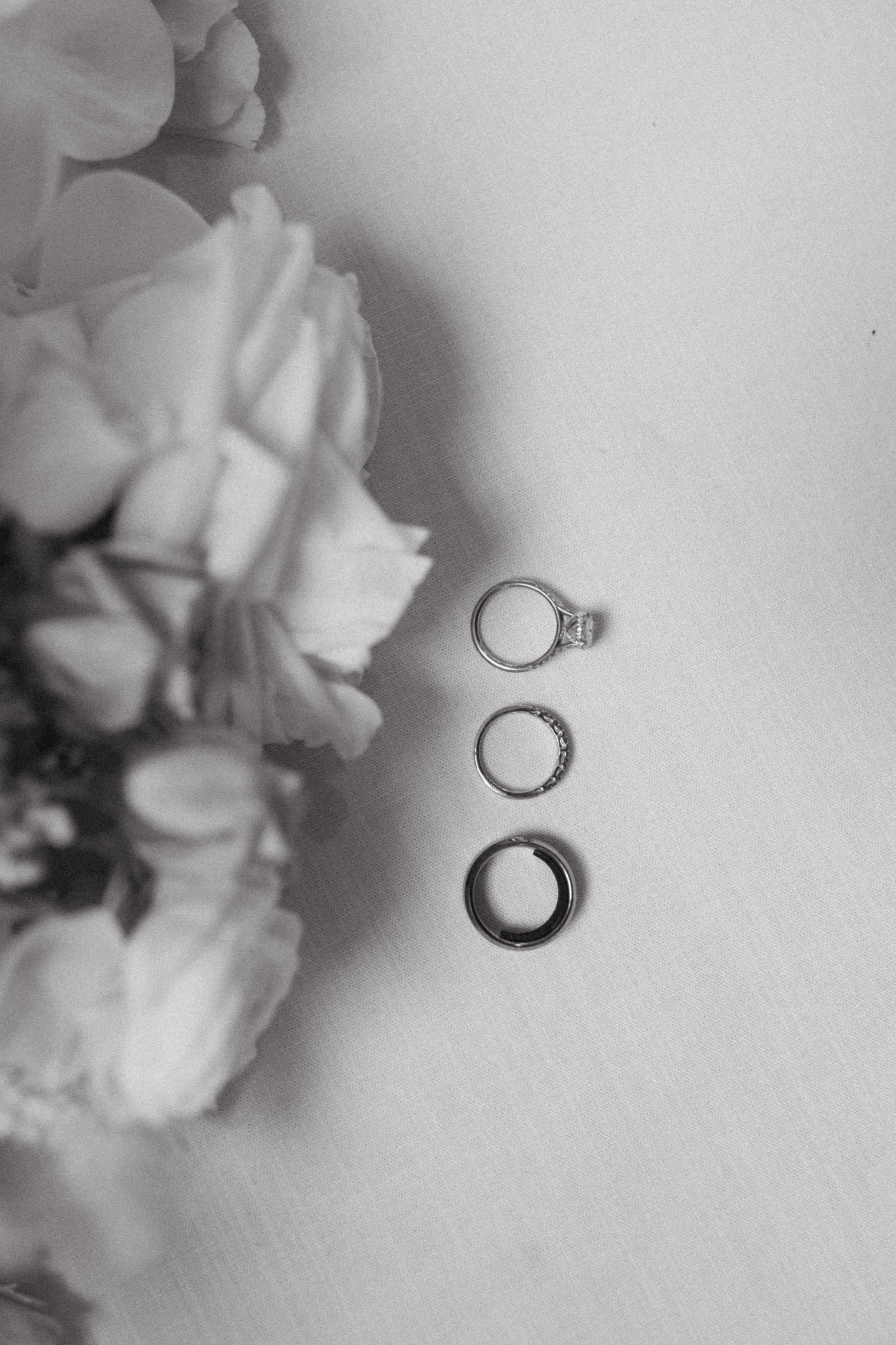 Three wedding rings arranged with soft floral elements in an elegant black and white composition.