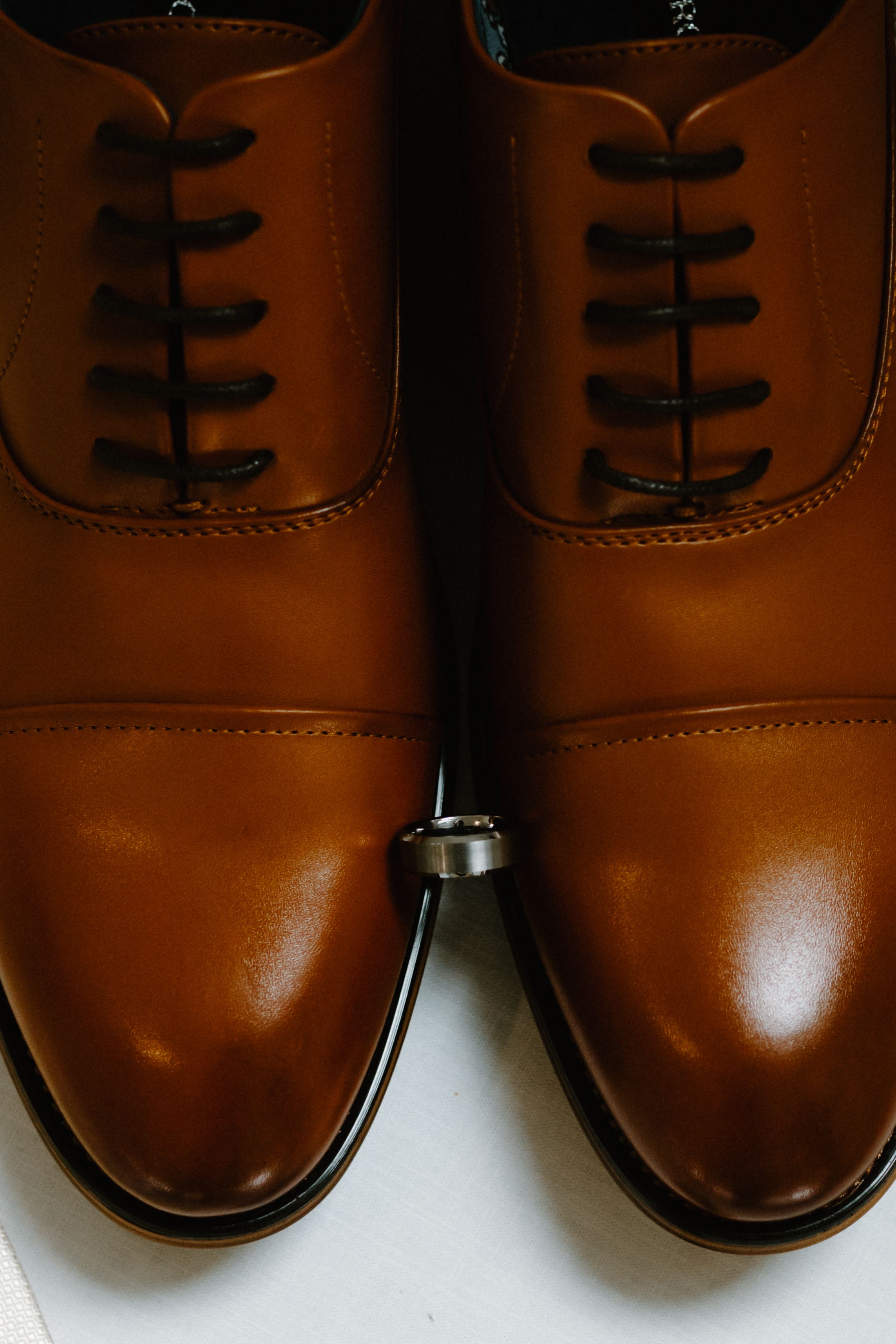 Classic brown leather oxford dress shoes with black laces photographed from above with a wedding ring between them.